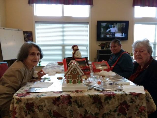 A group of people sitting around a table with a decorated gingerbread house, enjoying a festive gathering.