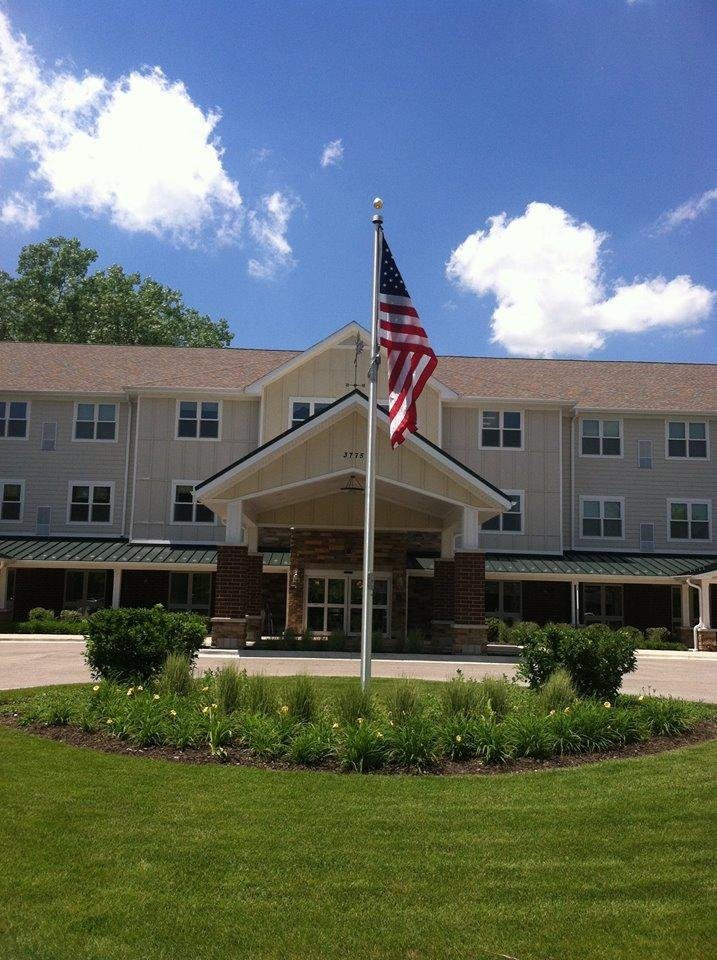 A large building with an American flag in front, surrounded by greenery under a clear sky.