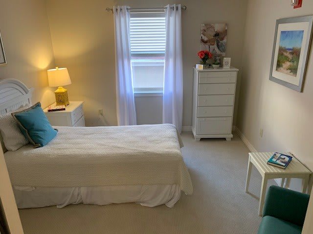 A neatly arranged bedroom with a bed, lamp, and dresser by the window.