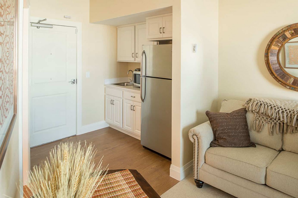 A cozy apartment corner featuring a small kitchen and living area with a refrigerator, couch, and modern decor.