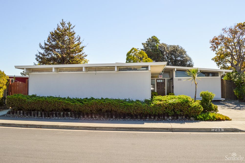 A modern, mid-century style home with a white exterior and surrounding greenery.