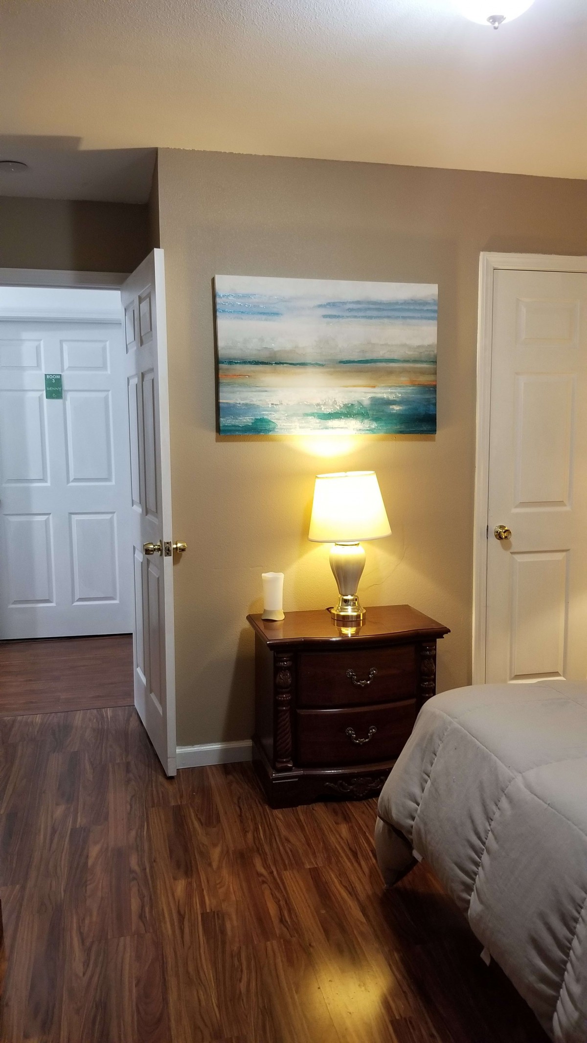 A cozy bedroom with a nightstand and lamp, featuring a painting above.