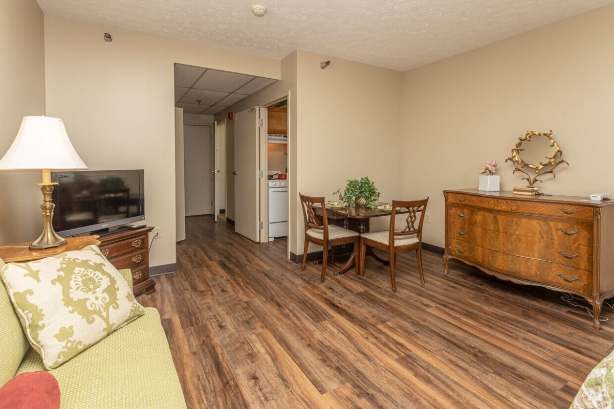 A cozy living and dining area with wood flooring, featuring a small dining table with chairs, a television, and additional furniture.