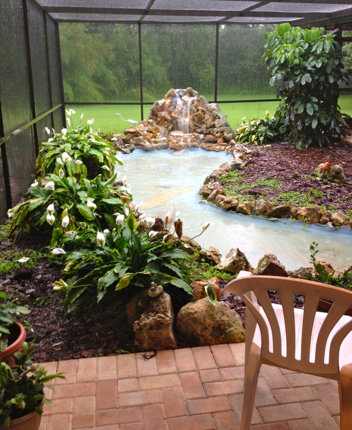 A serene garden with a small pond and lush greenery, adjacent to a patio area.