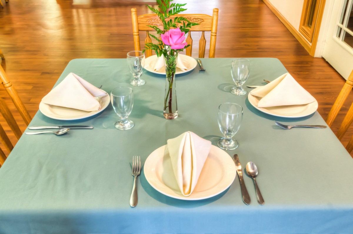 A neatly arranged dining table set for four, featuring folded napkins, glassware, and a floral centerpiece.