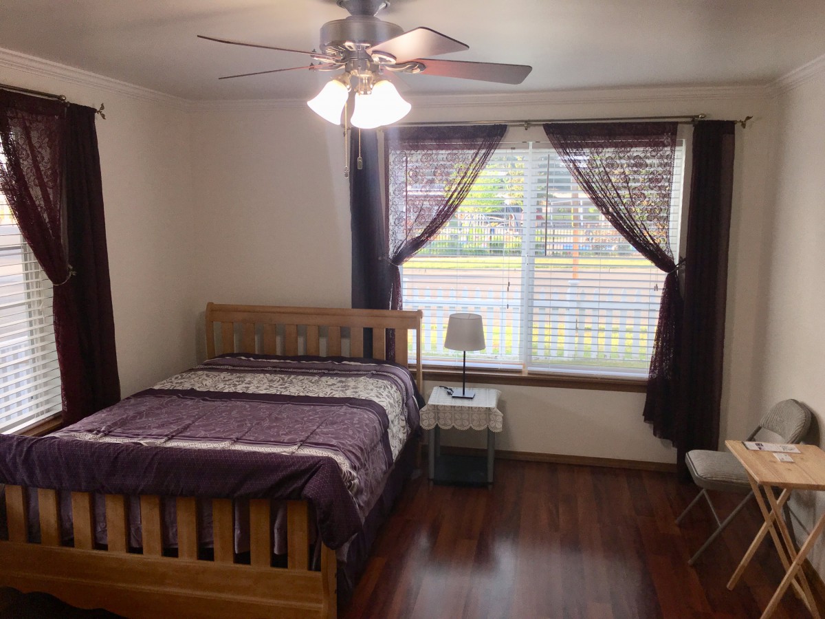 A cozy bedroom with a wooden bed, bedside lamp, and large window with curtains.