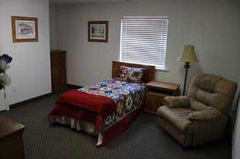 A small bedroom with a single bed, armchair, and nightstand next to a window.