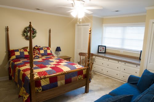 A cozy bedroom with a wooden bed and colorful quilt, alongside a dresser and table lamp.