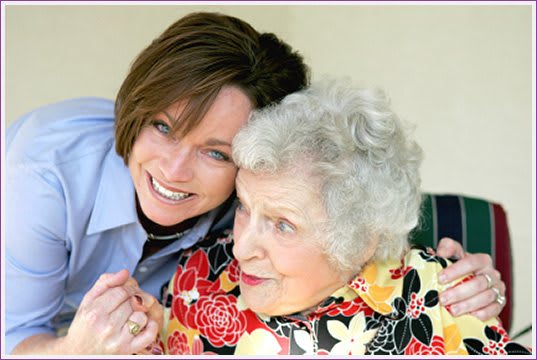 A joyful moment shared between two women, one elderly and one younger, as they smile and embrace each other.
