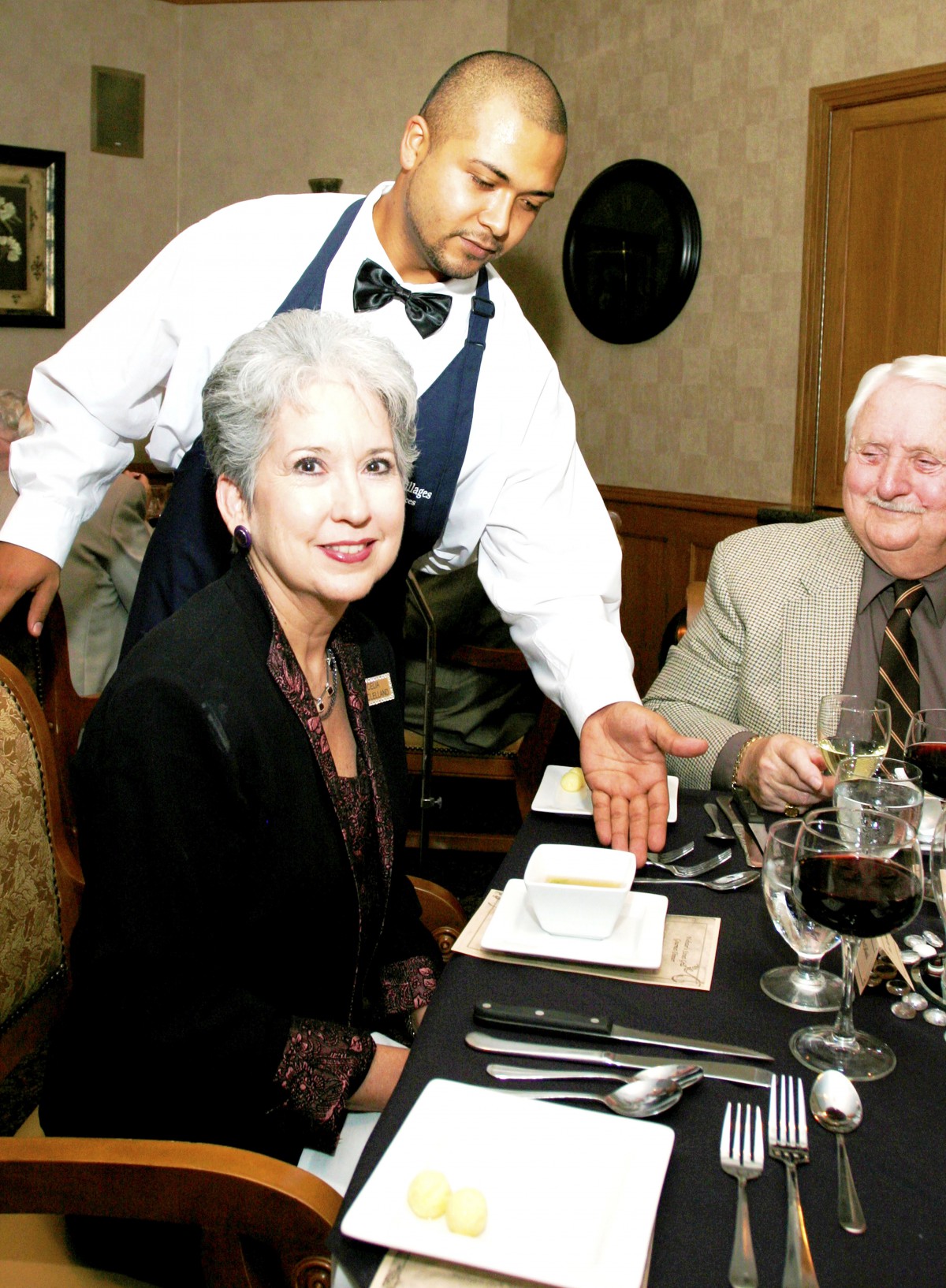 An elderly couple enjoying a meal at a restaurant while being served by a waiter.