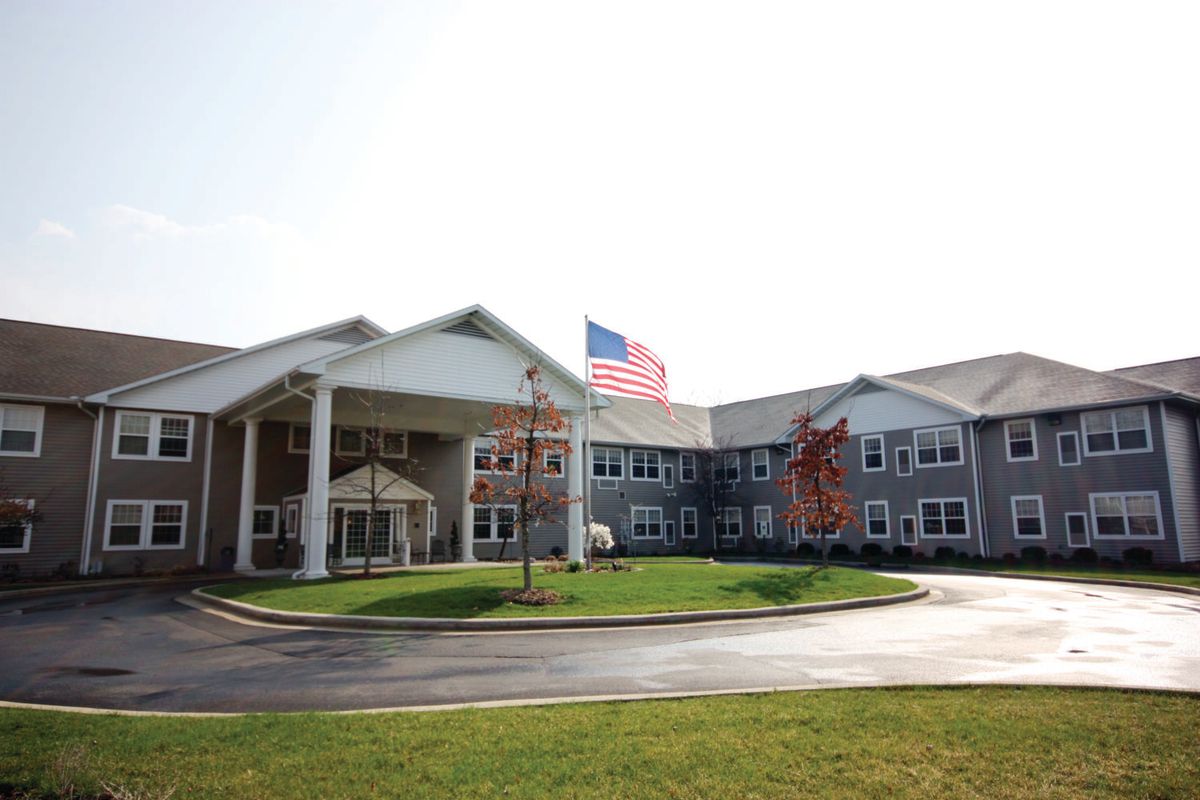 A large building with a U.S. flag, surrounded by manicured lawns and trees, under a clear sky.