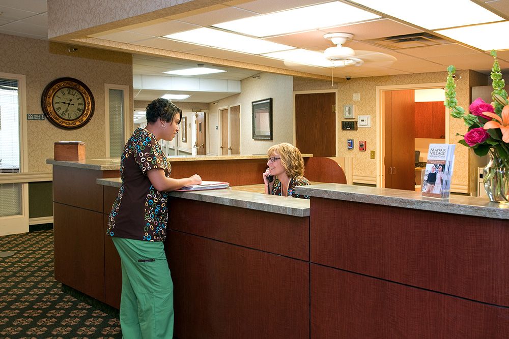 A nurse interacts with a receptionist at a hospital reception desk.