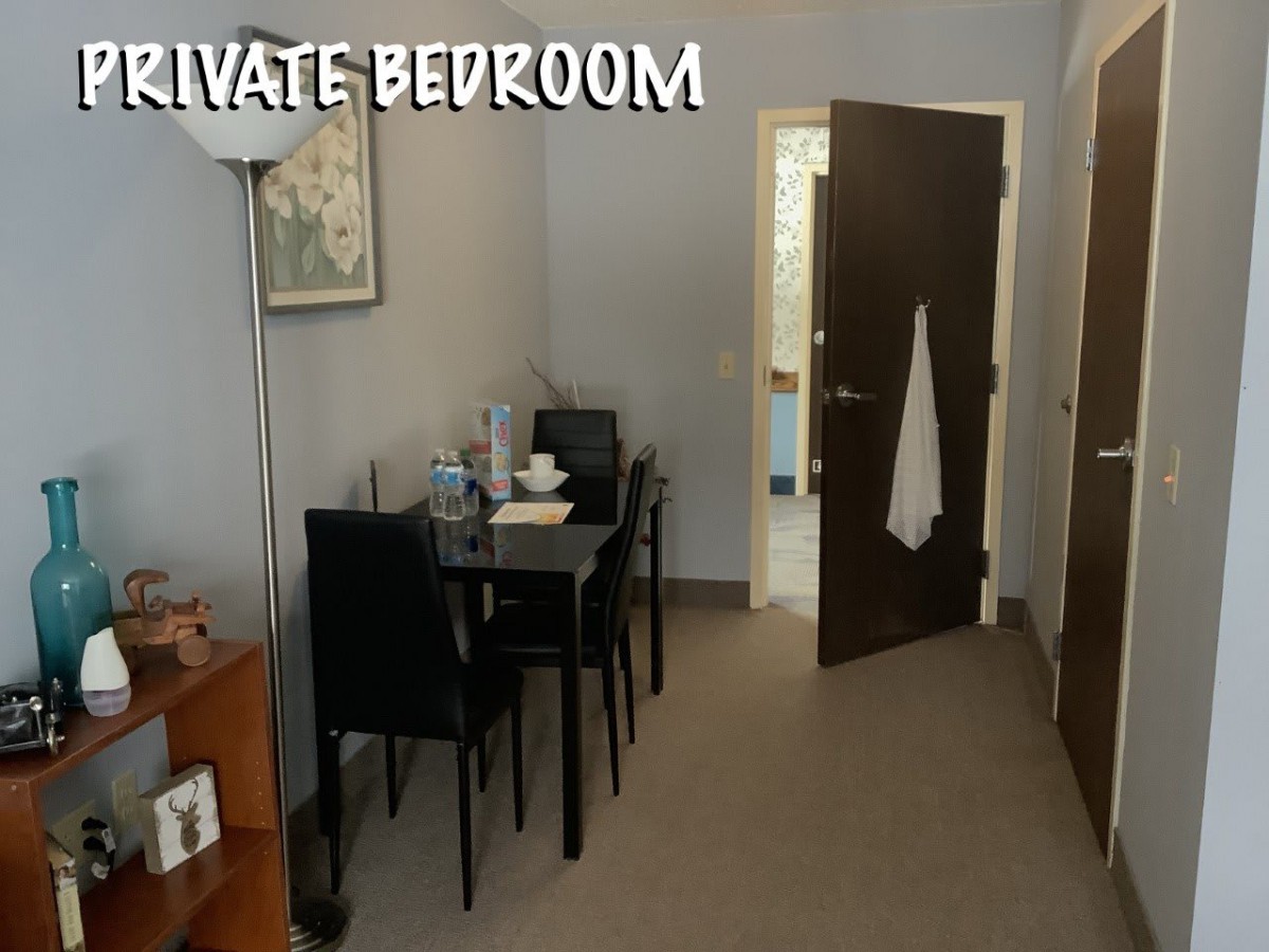 A cozy bedroom space featuring a small dining area, lamp, and open doorway.