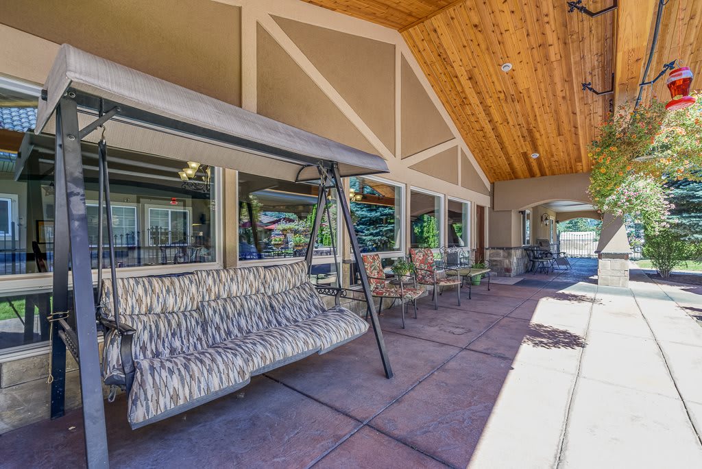 A cozy outdoor patio with a swing and seating area under a wooden ceiling.