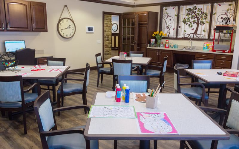An activity room with tables set up for arts and crafts, featuring chairs, art supplies, and wall decorations.
