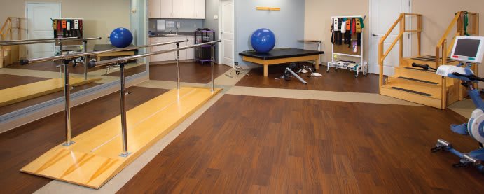 A physical therapy room equipped with exercise equipment and wood flooring.