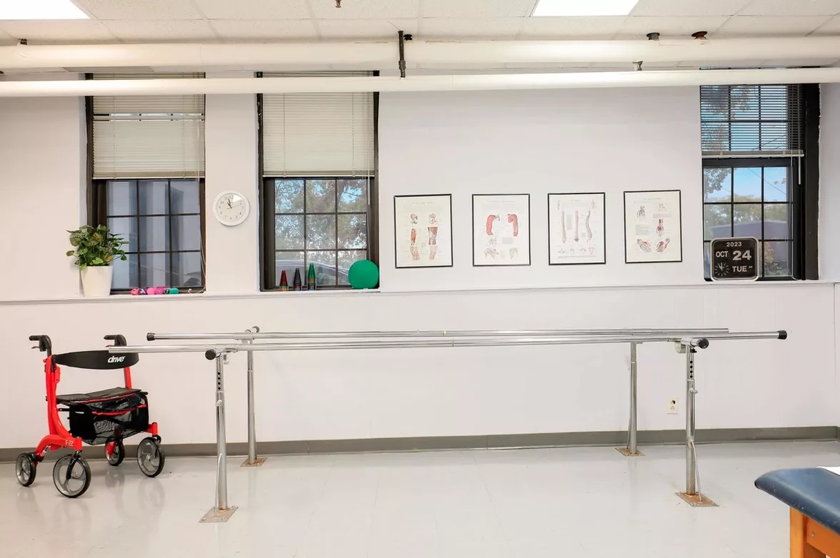 An empty dance studio with a ballet barre and framed artwork on the wall.