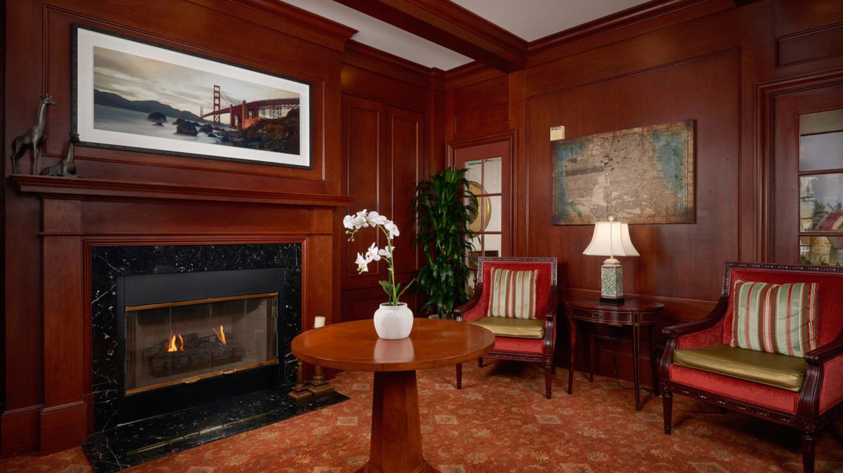 A cozy living room with wood paneling featuring a fireplace, armchair, and a small table with an orchid plant.