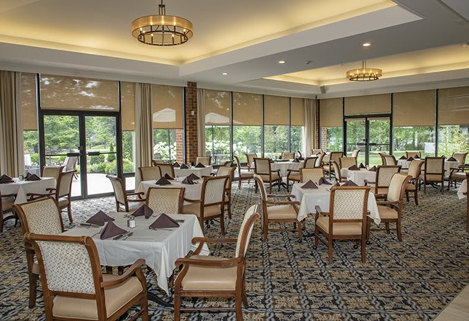 An elegant dining room with neatly arranged tables and chairs, featuring large windows and chandeliers.