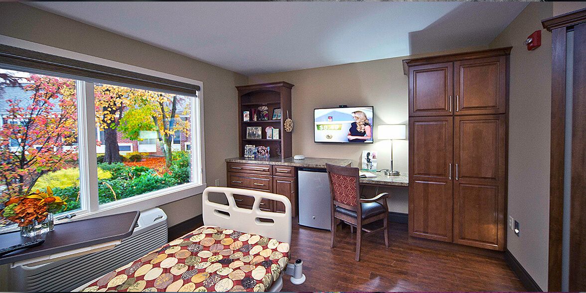 A well-furnished hospital room with a bed, desk, and television.