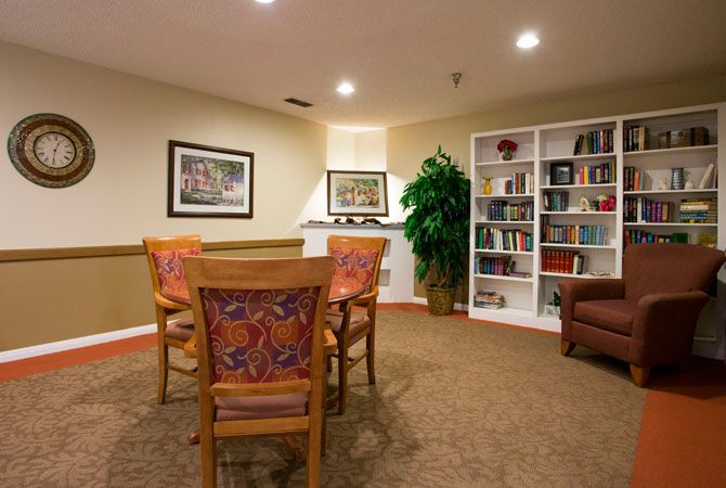 A cozy library room with a table and chairs, surrounded by bookshelves and artwork.