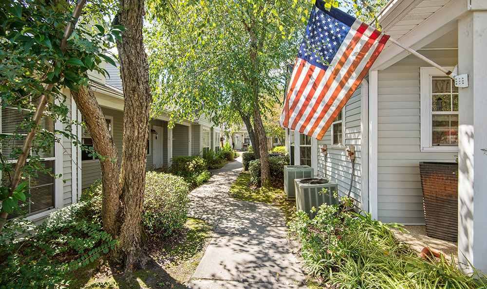 A peaceful residential pathway with an American flag displayed under the shade of trees.