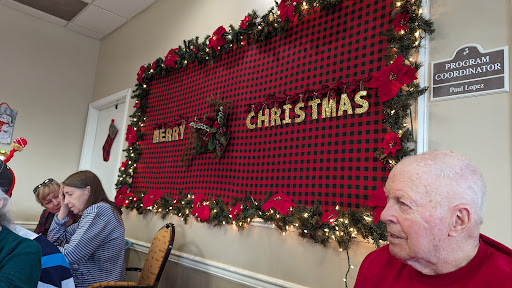A festive Christmas decoration featuring a 'Merry Christmas' sign adorned with red flowers and greenery.