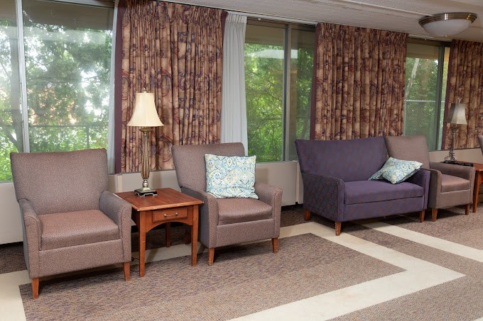 A cozy waiting area with chairs, a sofa, and lamps placed near large windows with drawn curtains.