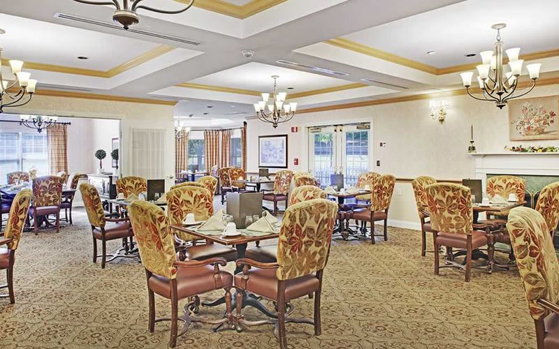 A well-decorated dining room with multiple tables and comfortable chairs, featuring elegant light fixtures.