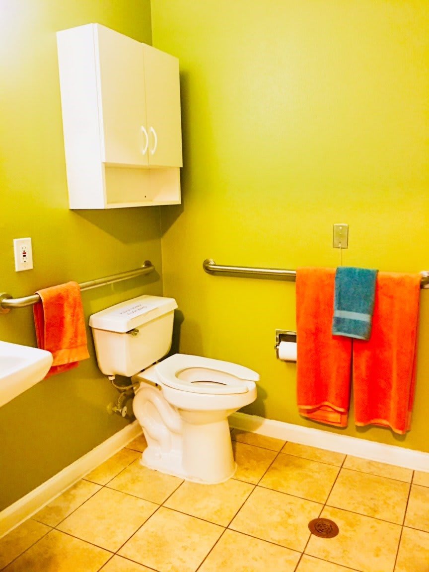 A brightly colored bathroom with green walls, featuring a toilet, sink, and orange towels.
