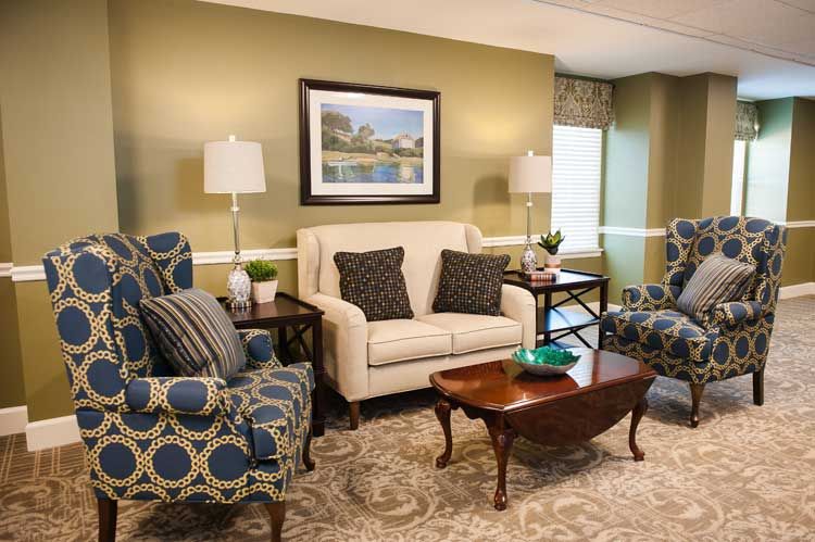 A cozy living room with a sofa, armchairs, and a coffee table, decorated with lamps and artwork.