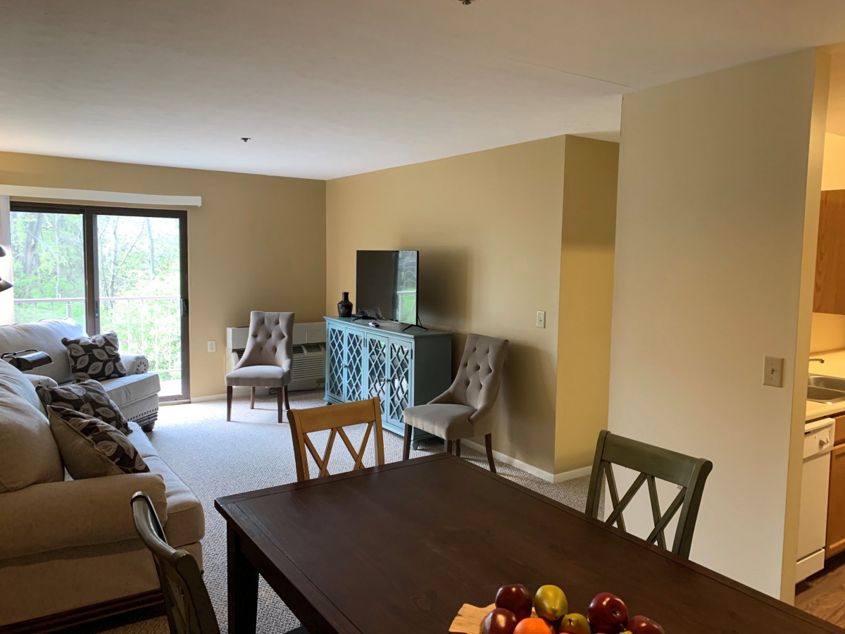 A cozy living and dining area with neutral tones, featuring a TV, seating, and a dining table.