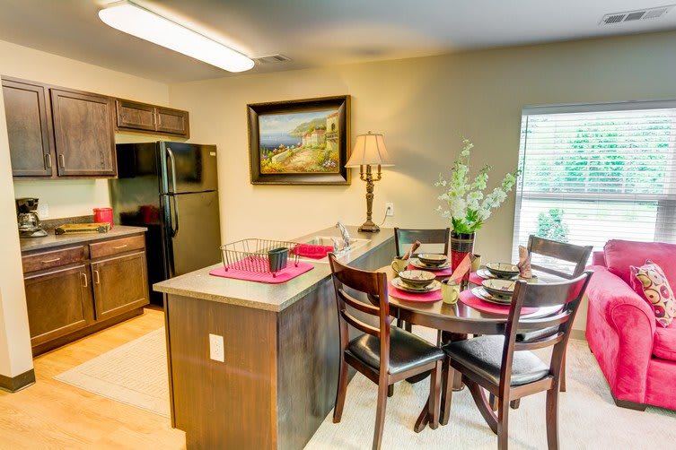 A cozy kitchen and dining area with a table set for four, featuring a modern design with wooden cabinets and bar stools.