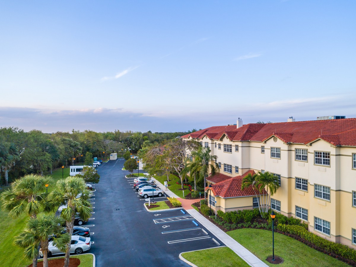 Aerial view of an apartment complex with a parking lot and surrounding greenery.