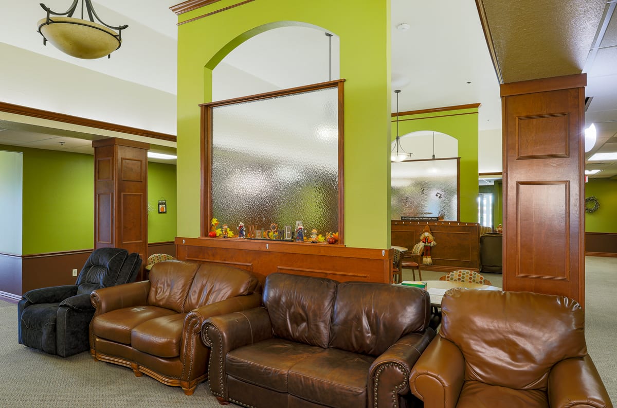 A cozy waiting area with leather couches and green walls, featuring a frosted glass partition.