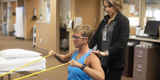 A person participating in physical therapy using resistance bands, guided by a therapist.