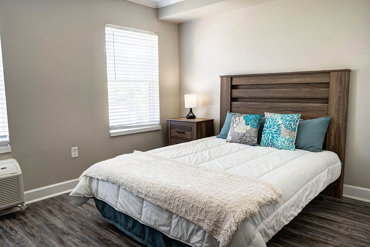 A cozy bedroom with a neatly made bed, colorful pillows, and a lamp on the nightstand.