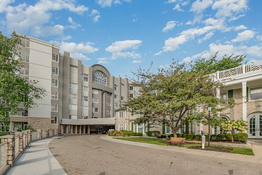 A modern multi-story building surrounded by greenery under a bright blue sky.