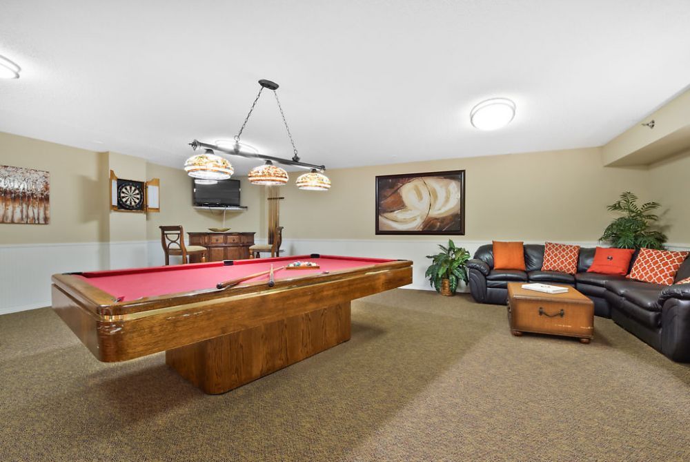 A cozy billiard room with a red-felt pool table and comfortable seating, accentuated by warm lighting and decorative artwork.