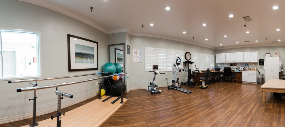 A well-equipped rehabilitation gym with exercise machines, fitness balls, and parallel bars for physical therapy.