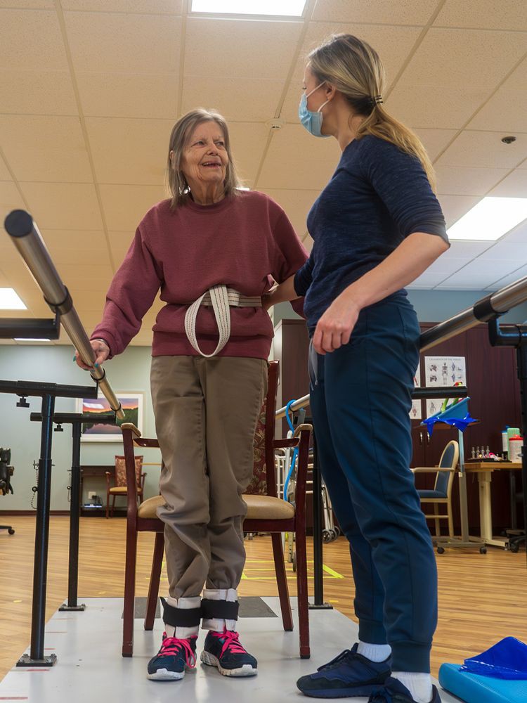 An elderly woman receives assistance from a healthcare professional during a physical therapy session.