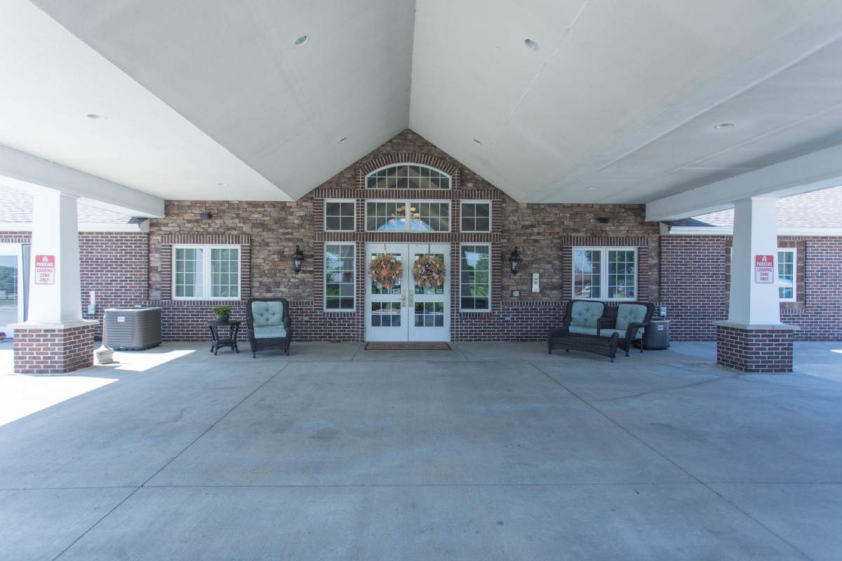 The image shows the entrance of a brick building with multiple windows and seating arrangements outside.