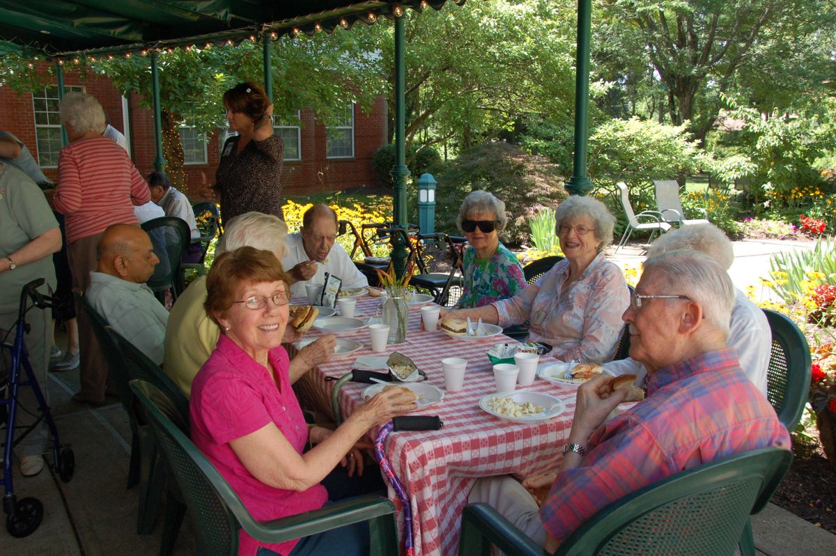 A group of people enjoying an outdoor gathering around a table in a garden setting.