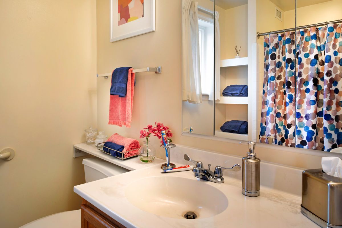A neatly arranged bathroom with colorful towels, a floral arrangement, and a decorative painting above the towel rack.
