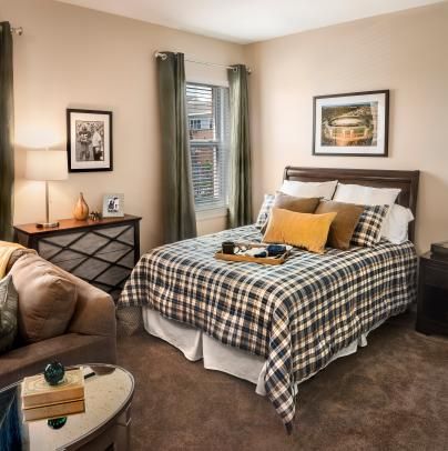A cozy bedroom features a plaid-patterned bed, accompanying sofa, stylish artwork, and inviting decor.