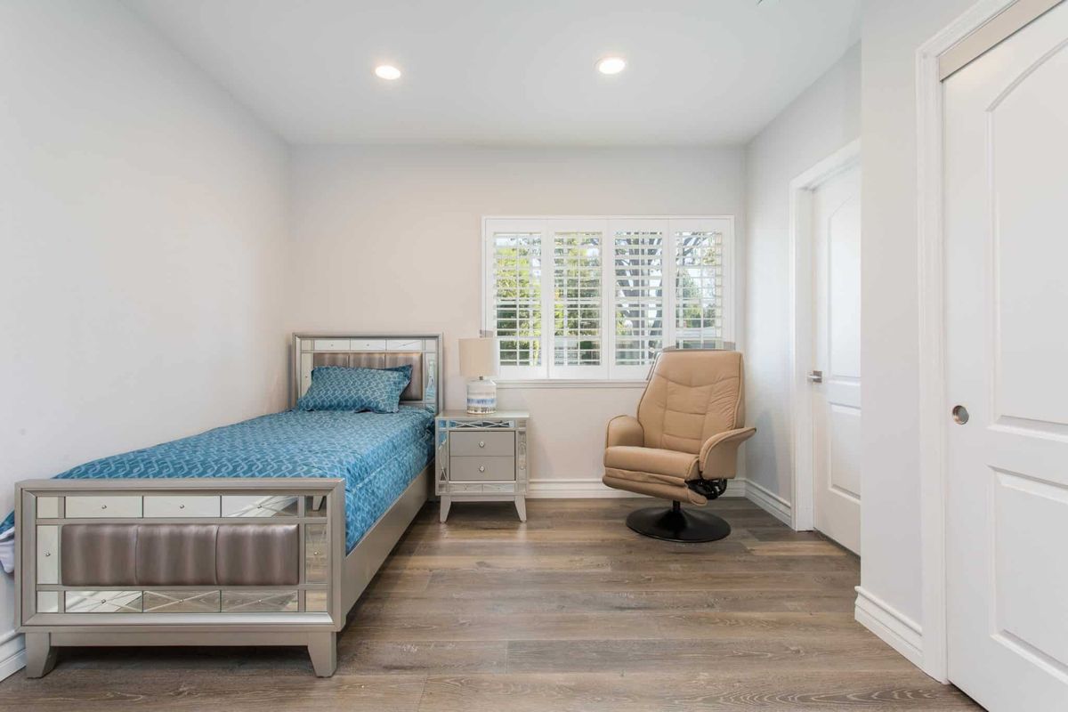 A minimalist bedroom with a single bed, wooden flooring, and a chair by the window.
