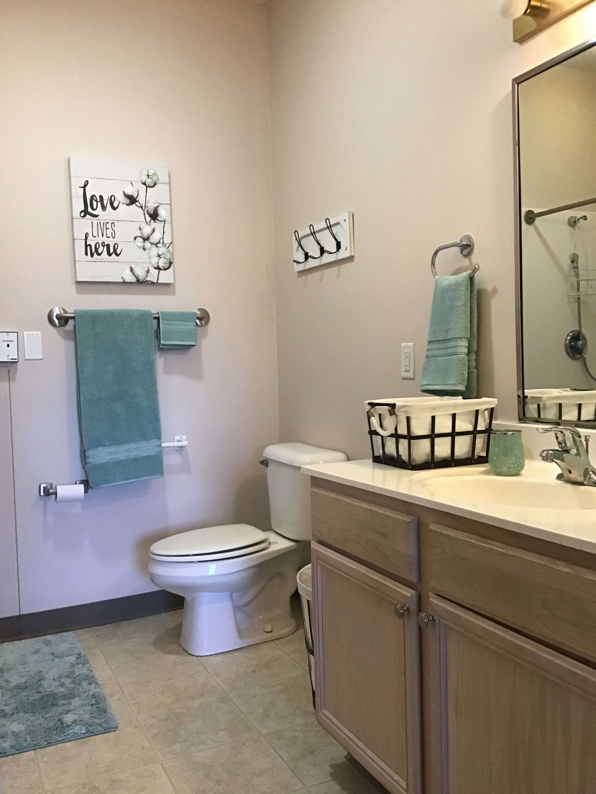 A clean, organized bathroom with teal towels and simple decor.