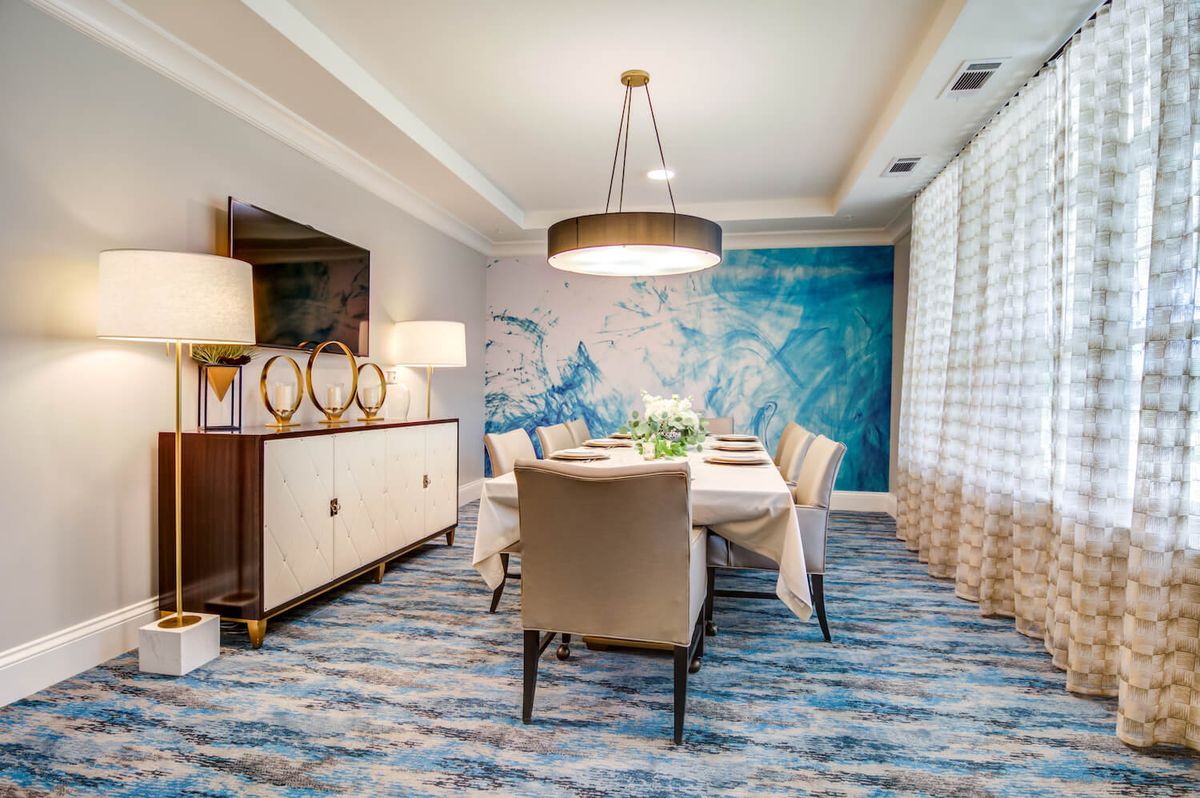 A stylish dining room featuring modern furniture, decorative wall art, and contemporary lighting with an elegant carpeted floor.