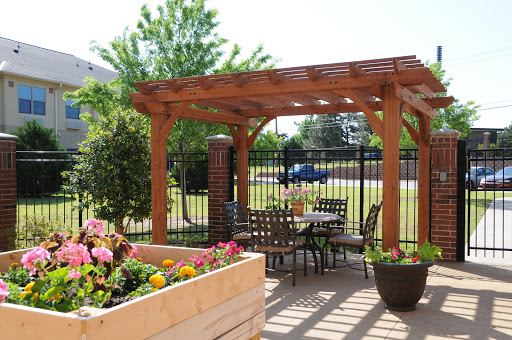 A serene outdoor patio area featuring a wooden pergola, seating arrangements, and vibrant flower beds.