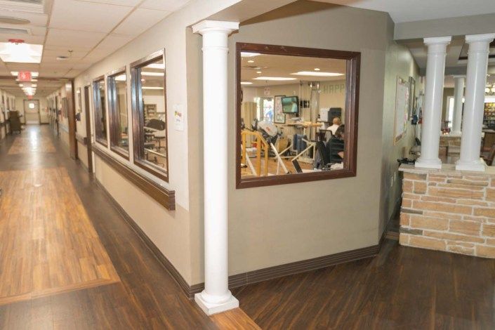 A corridor in a rehabilitation center featuring gym equipment visible through large windows.